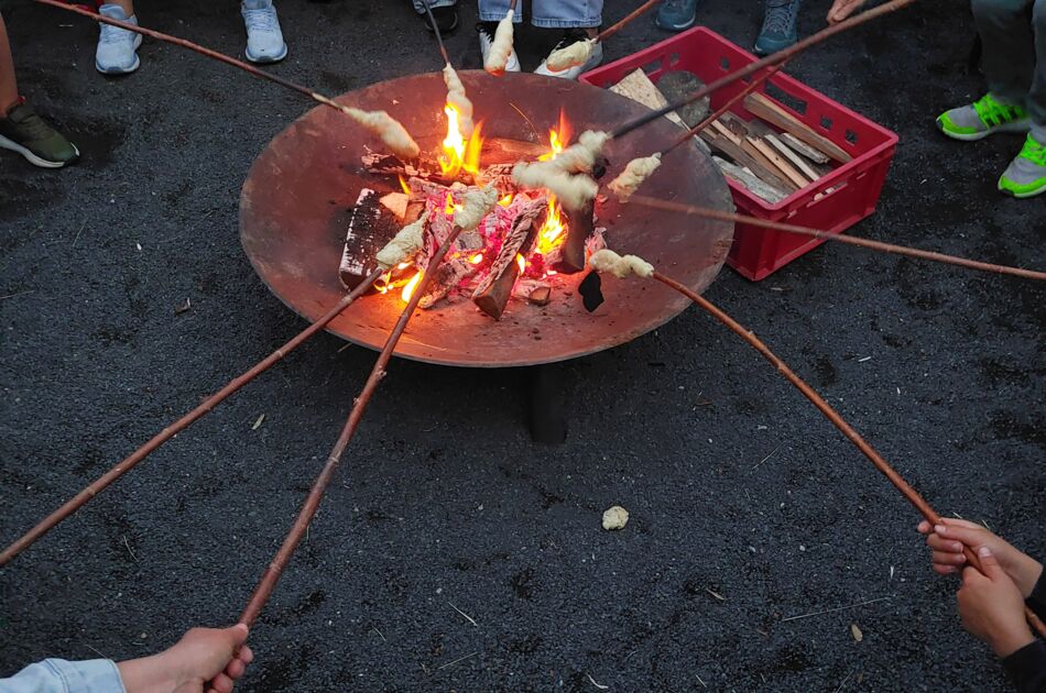 Mehrere Menschen halten Stöcke mit Stockbrot in eine brennende Feuerschale